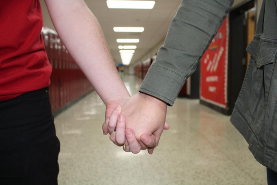 Two students holding each others hand in an empty school hallway.