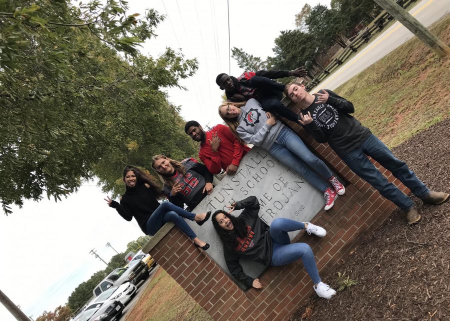 The 2019-2020 Trojan Messenger sign posing in front of Tunstall High School sign.