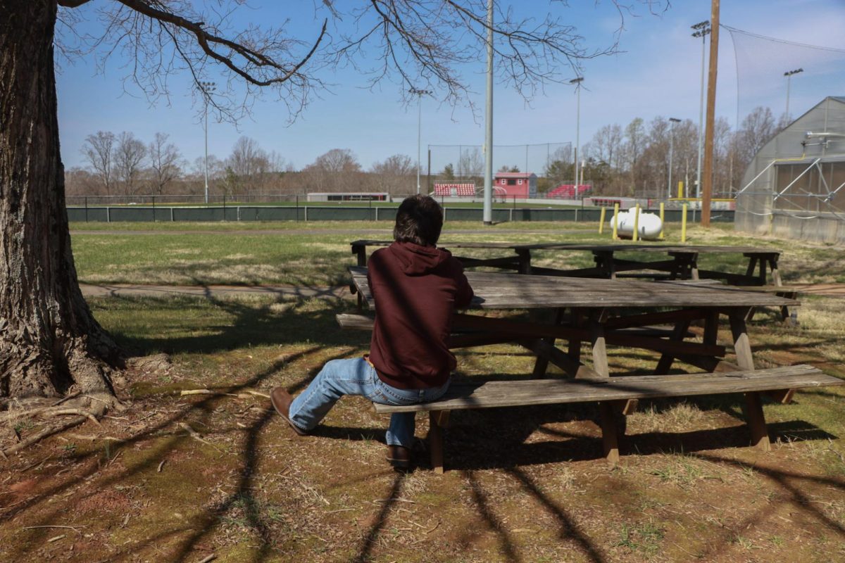 Senior Mason Clark sitting on a bench isolated from others. 