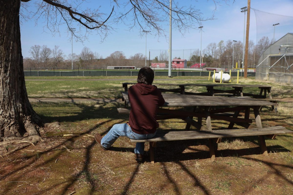 Senior Mason Clark sitting on a bench isolated from others.